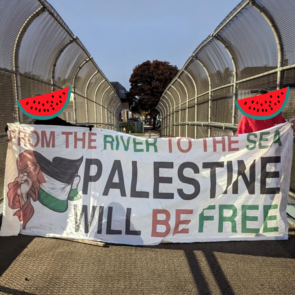People walk across a bridge with a banner reading "From the river to the sea Palestine will be free"