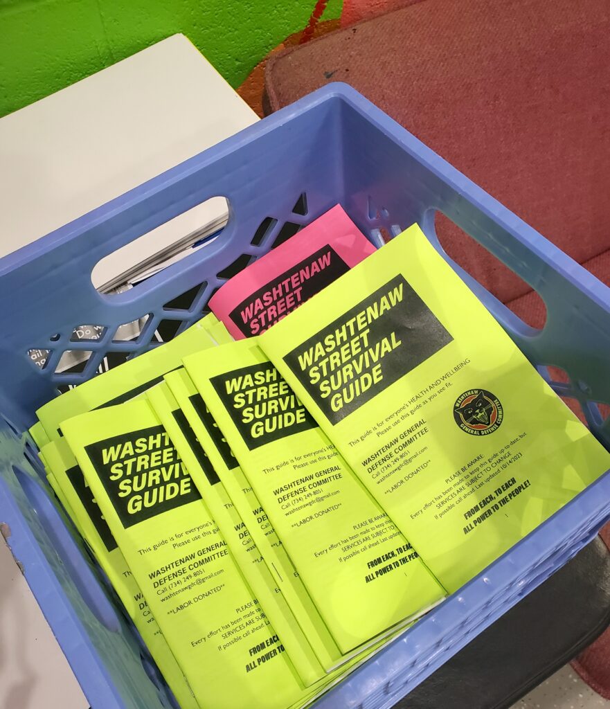 A crate full of colorful printed booklets that read "Washtenaw street survival guide"